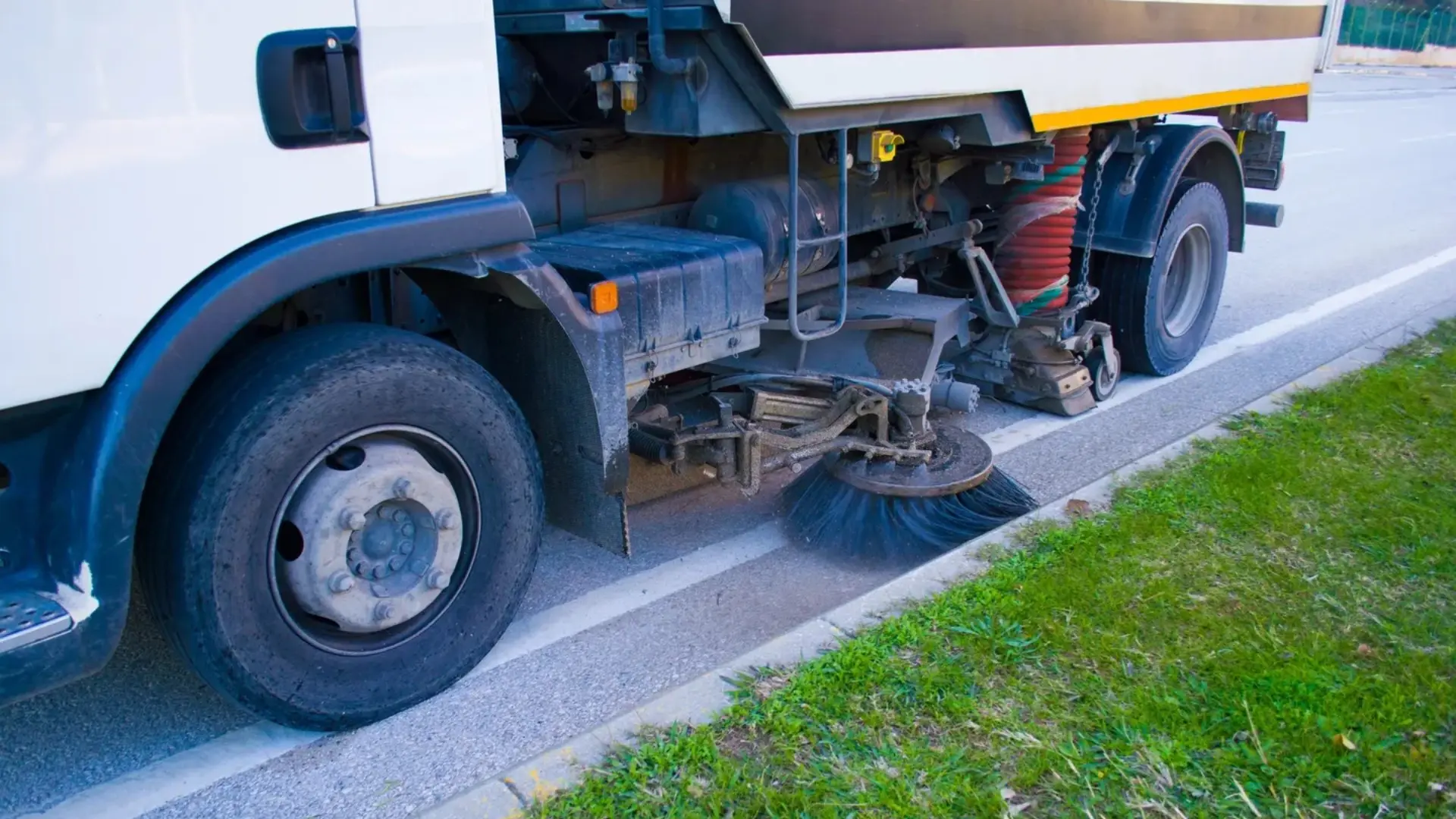 Street sweeper truck cleaning roadside pavement.