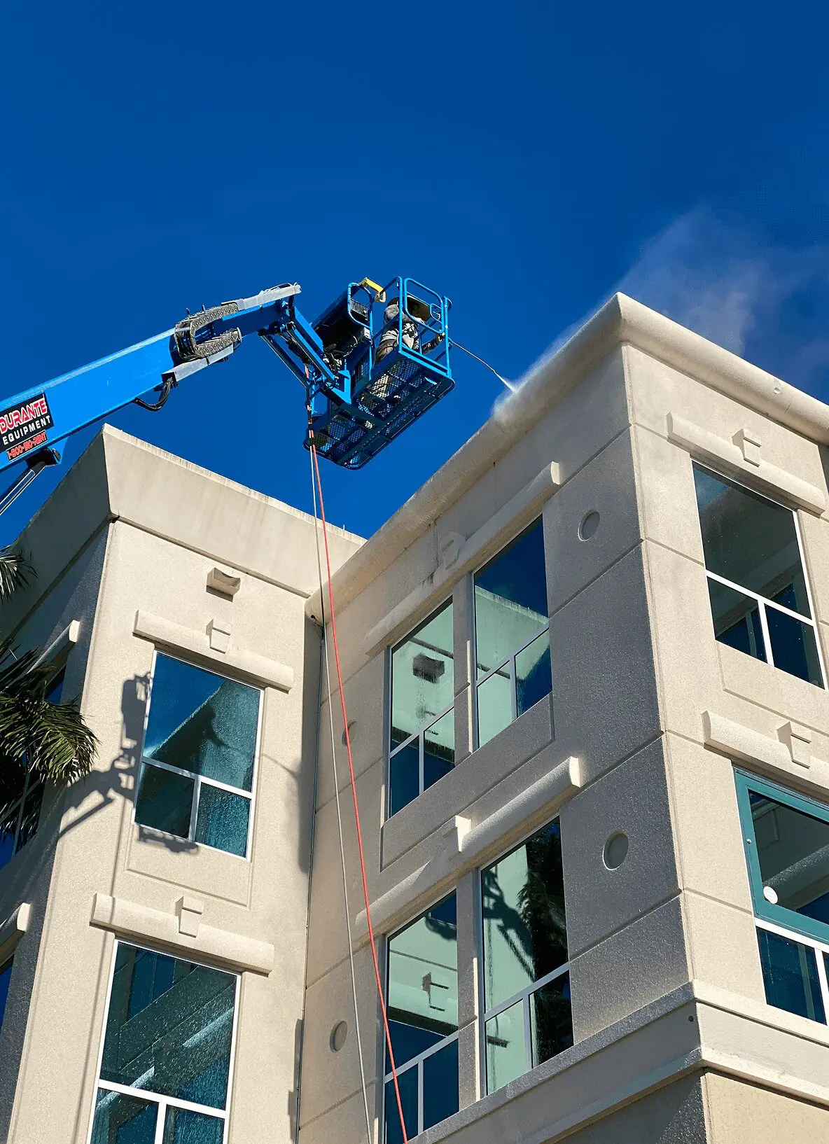 Crane cleaning windows on modern building exterior.